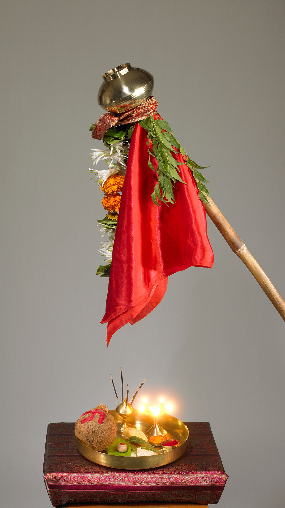 Traditional Gudi Padwa setup featuring a decorated Gudi with a red cloth, mango leaves, and a brass pot, alongside a puja thali with offerings and lit diyas.