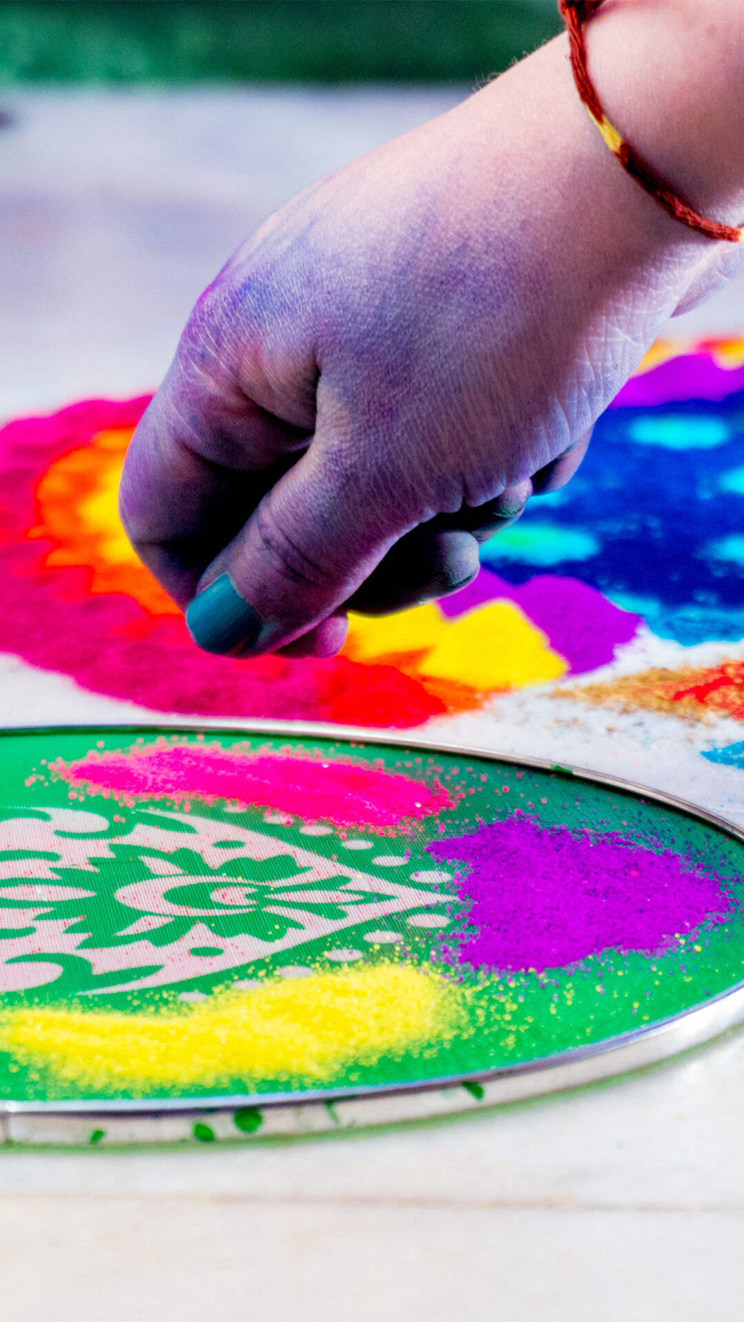 A beaHand creating a colorful Ugadi rangoli using a stencil, with vibrant sand powders forming intricate festive patterns.utiful Ugadi Rangoli