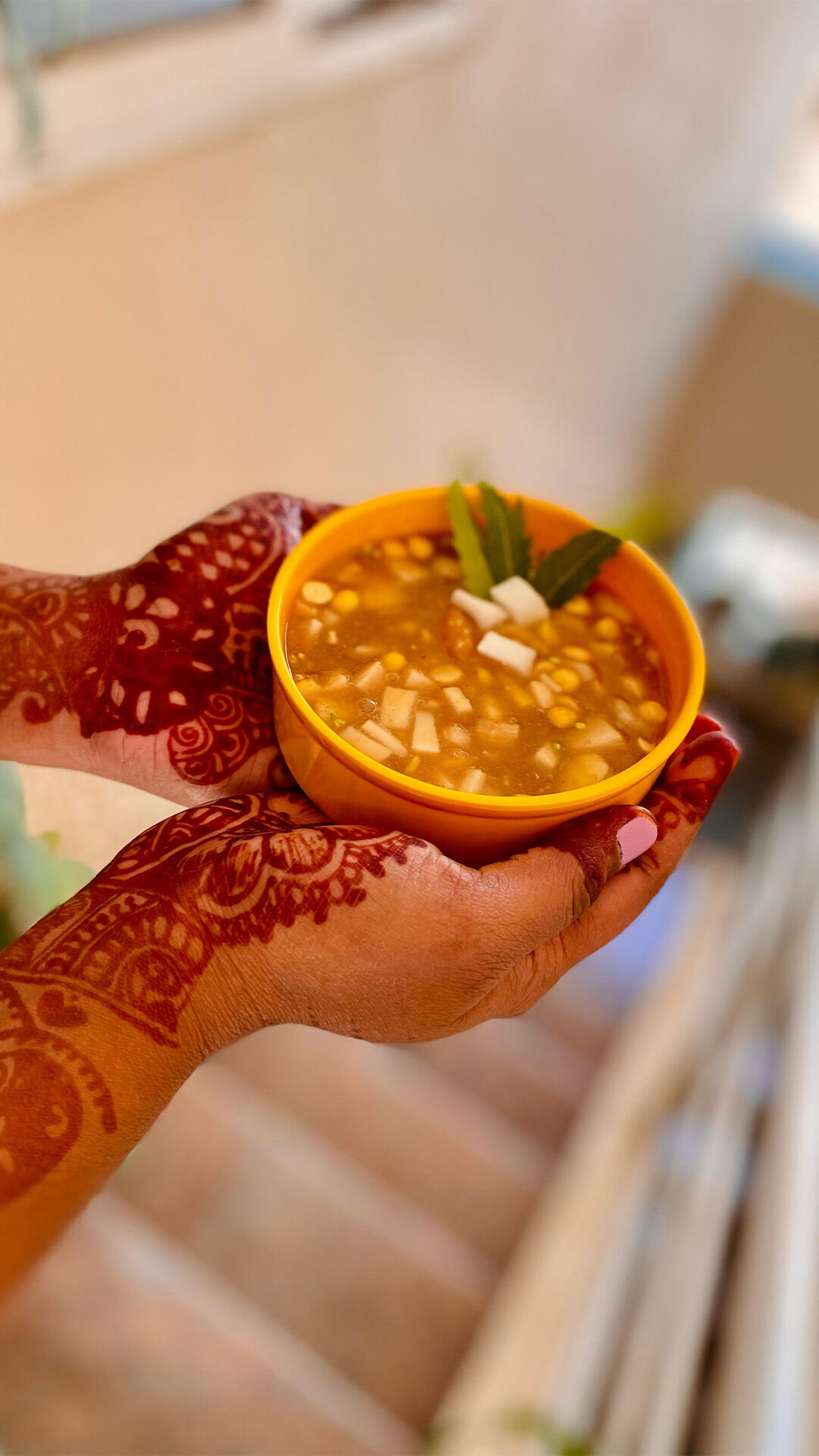 Hands adorned with intricate henna designs holding a bowl of Ugadi Pachadi, a traditional festive dish made with raw mango, jaggery, tamarind, and spices.