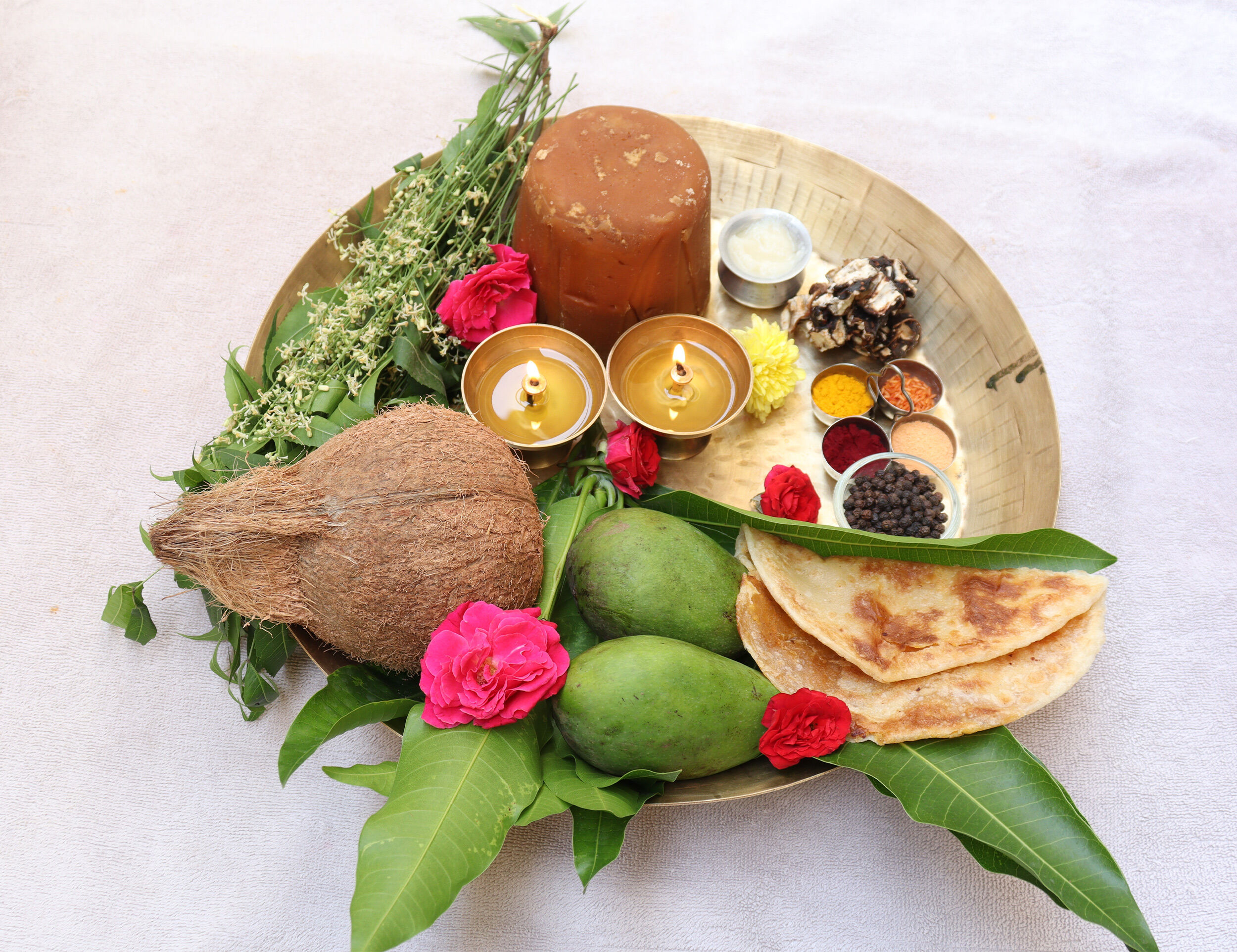 Traditional Ugadi festival puja thali with coconut, raw mangoes, jaggery, betel leaves, spices, lit diyas, and festive offerings.