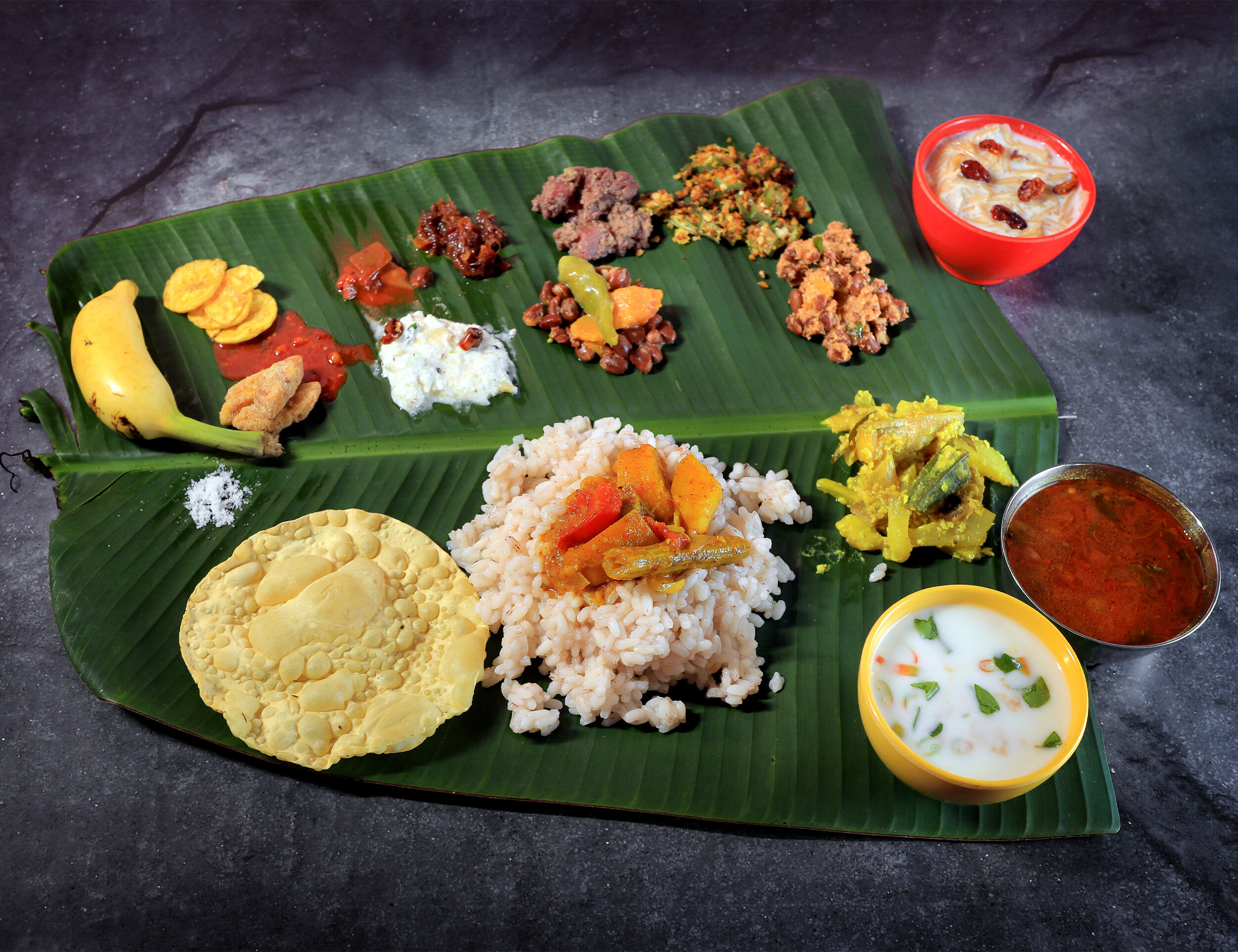 Traditional Kerala Sadya meal served on a banana leaf, featuring rice, sambar, avial, thoran, pickles, banana chips, papadam, and payasam for Vishu festival celebration