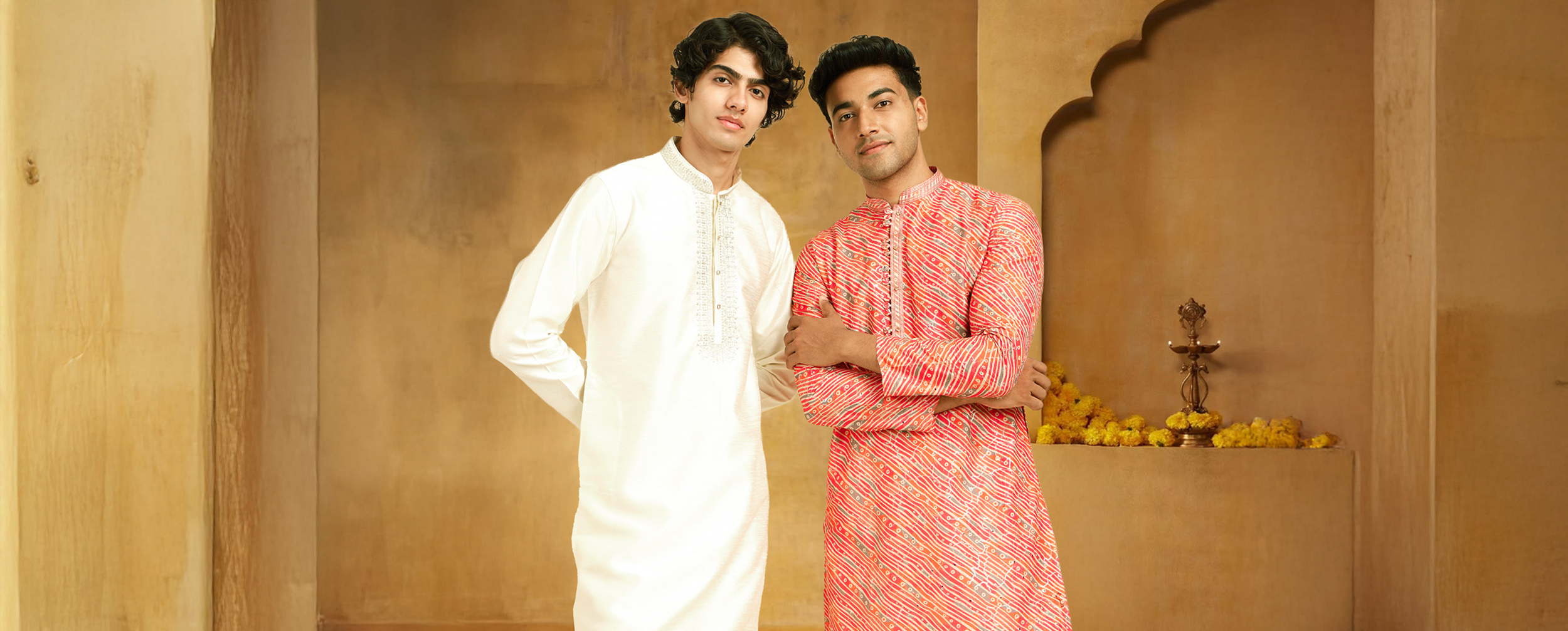 Two men in traditional red and white kurta pajamas posing against a festive background, representing the symbolic colors of Durga Puja.