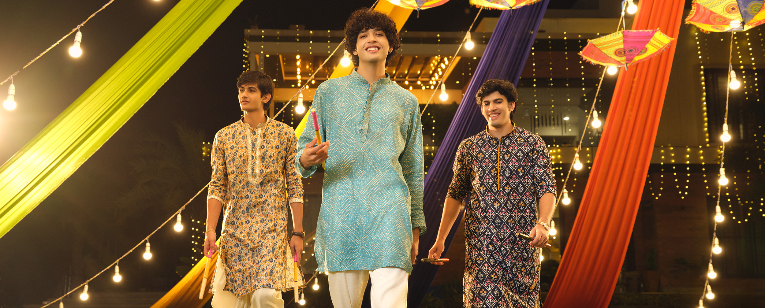 Group of young men wearing colorful festive kurtas, celebrating together outdoors.