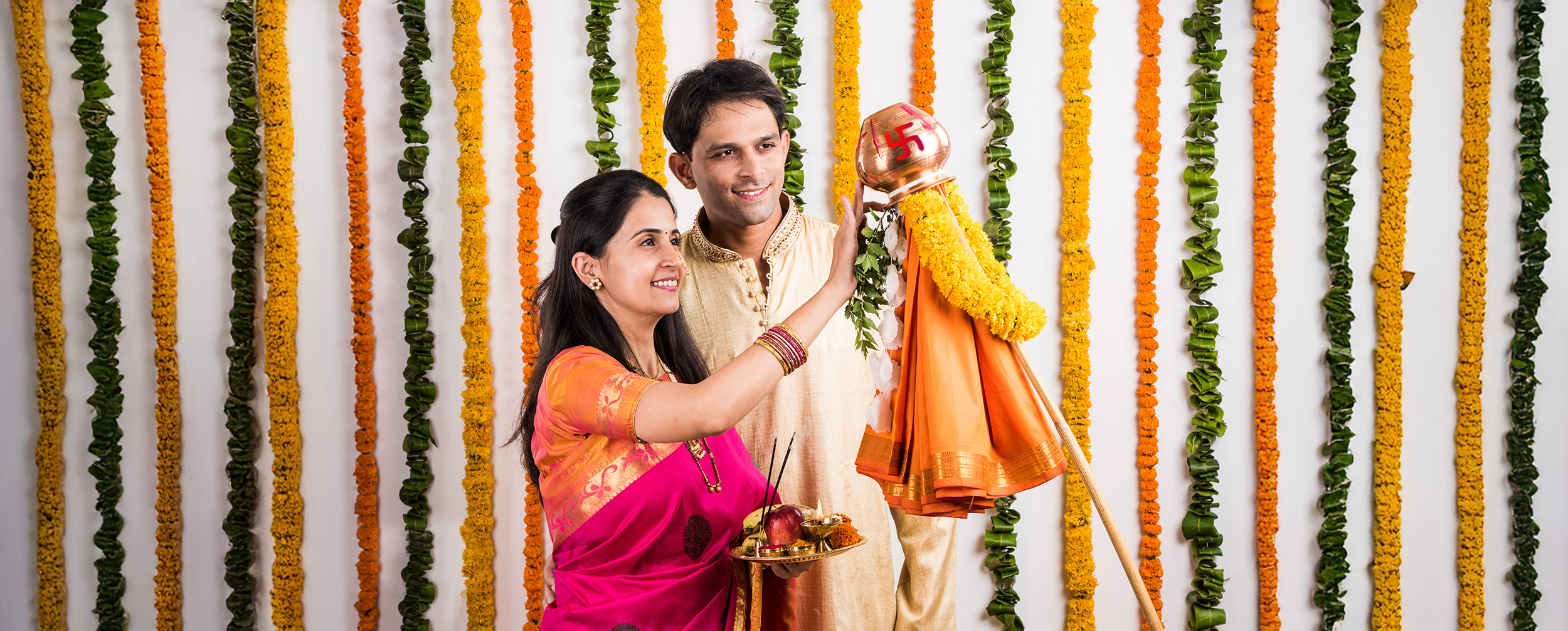 Happy couple celebrating Ugadi by performing the Gudi Padwa ritual, dressed in traditional attire with a decorated Gudi and festive floral backdrop. Happy couple celebrating Ugadi by performing the Gudi Padwa ritual, dressed in traditional attire with a decorated Gudi and festive floral backdrop.