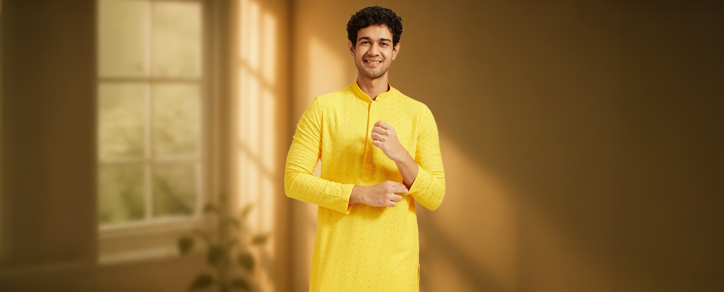 Man in vibrant yellow textured kurta standing in a warmly lit room with a potted plant by the window, showcasing festive ethnic fashion for men