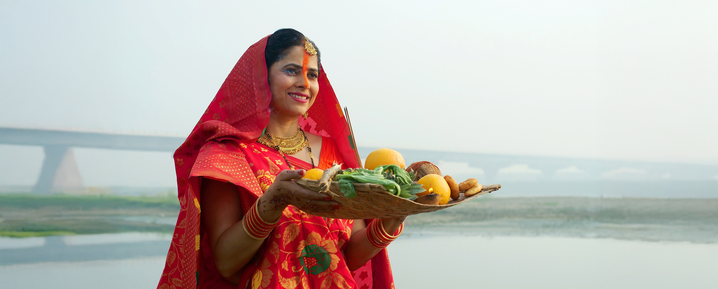 A devout woman in a red saree performing the solemn water worship and ritual during Chhath Puja.