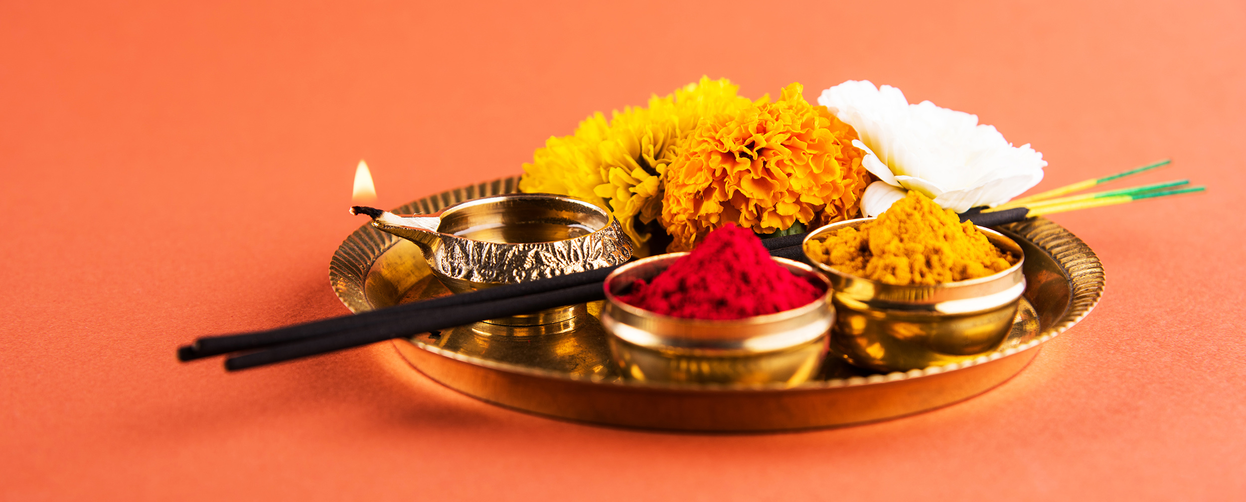 Traditional Indian pooja thali with marigold flowers, red and yellow gulal, incense sticks, and diya for festive rituals.