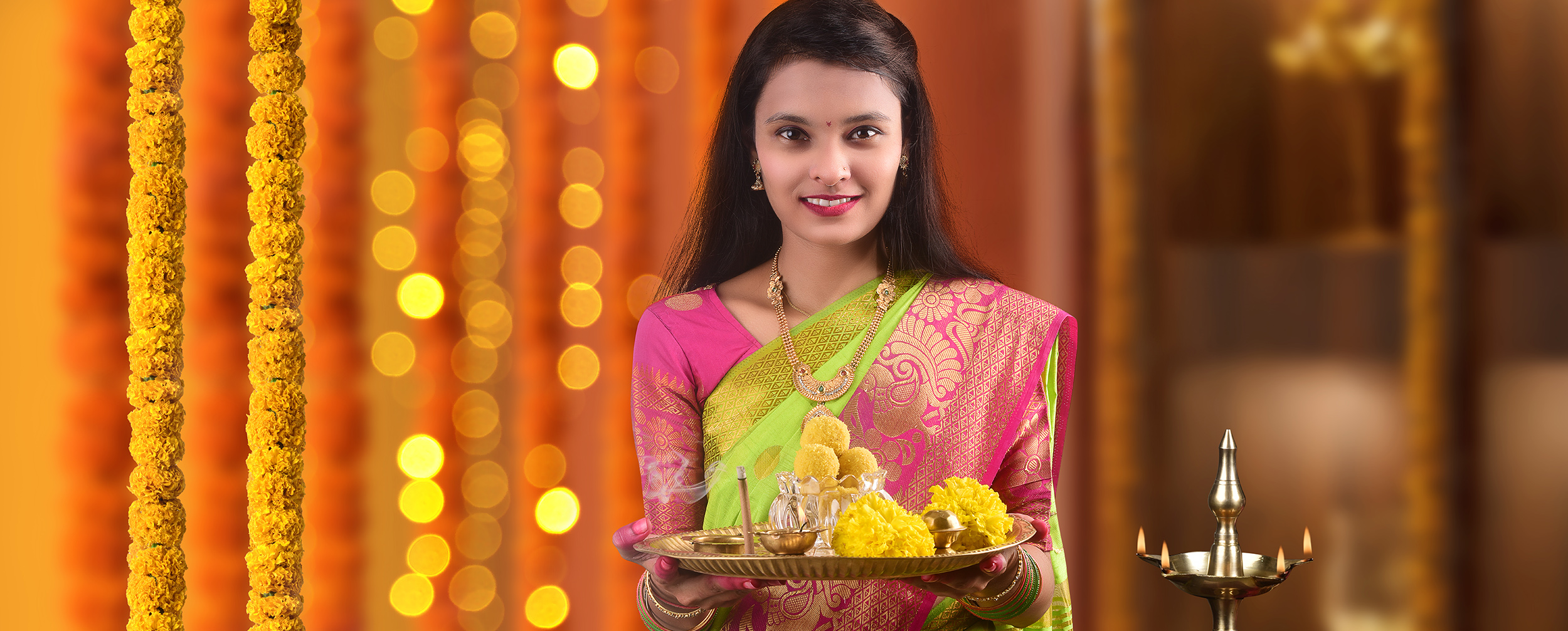 Smiling Indian woman performing a ritual for Durga Puja, holding a plate with traditional offerings like laddoo and marigold flowers.