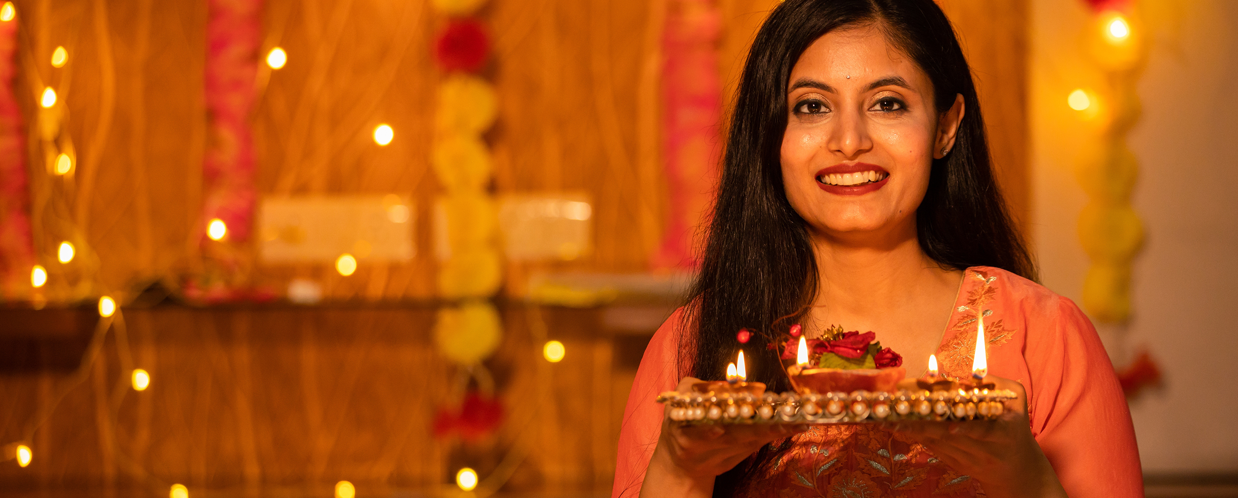 A woman holding a tray of lit diyas, ready for a radiant and joyful Diwali celebration. A woman holding a tray of lit diyas, ready for a radiant and joyful Diwali celebration.